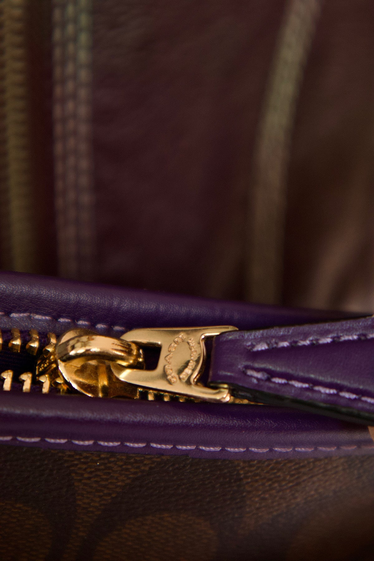 Détail fermeture éclair dorée avec finition cuir mauve sur sac Coach