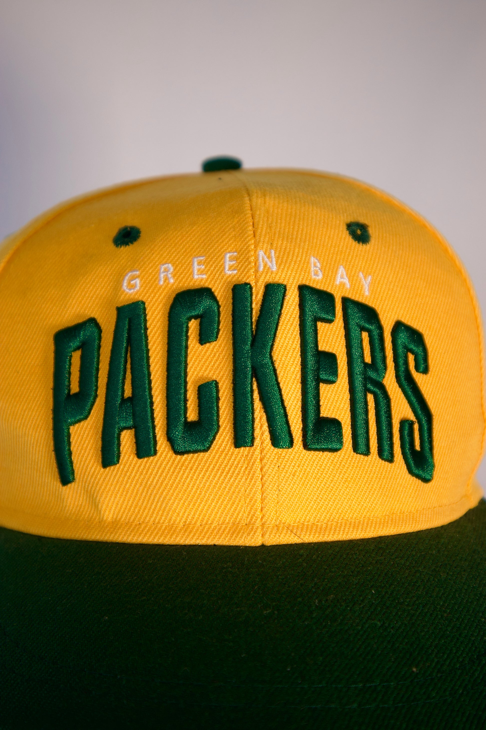 Détail logo Packers brodé en vert sur casquette jaune, style vintage NFL